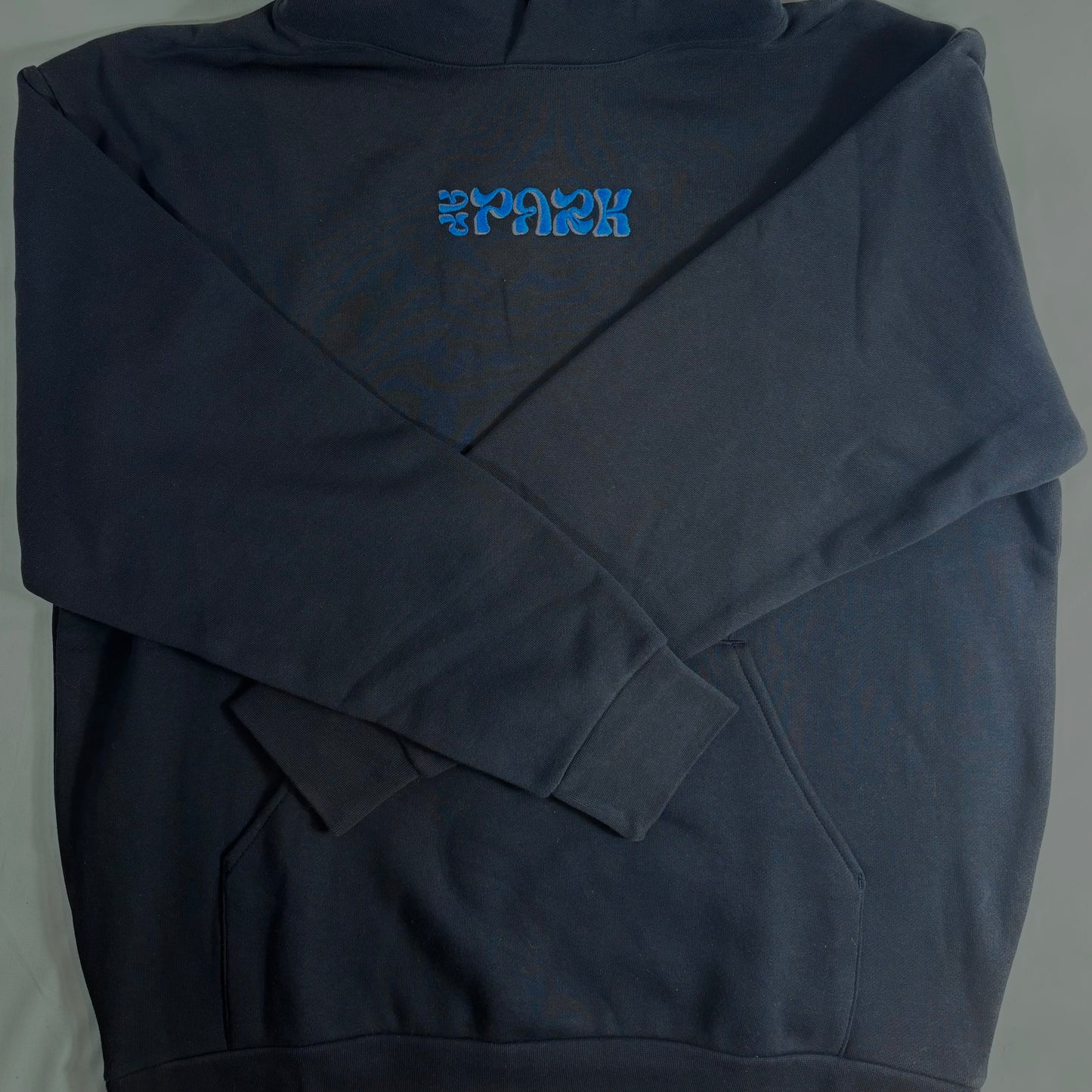 A folded navy blue hoodie with a bright blue stylized logo printed on the chest, laid flat against a light gray background.