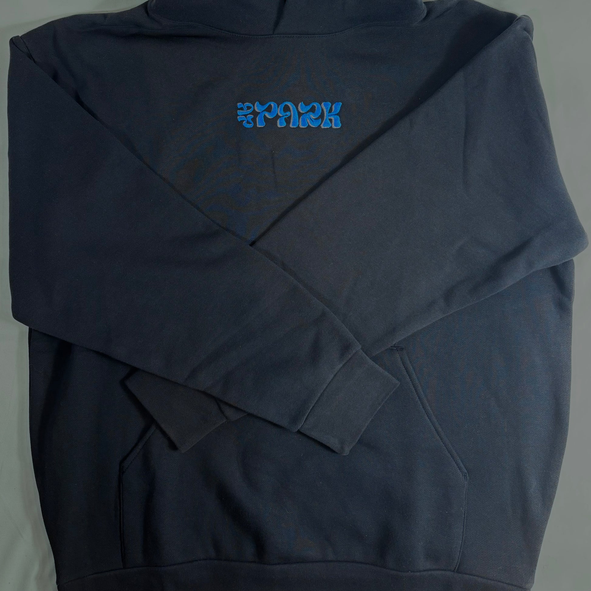 A folded navy blue hoodie with a bright blue stylized logo printed on the chest, laid flat against a light gray background.